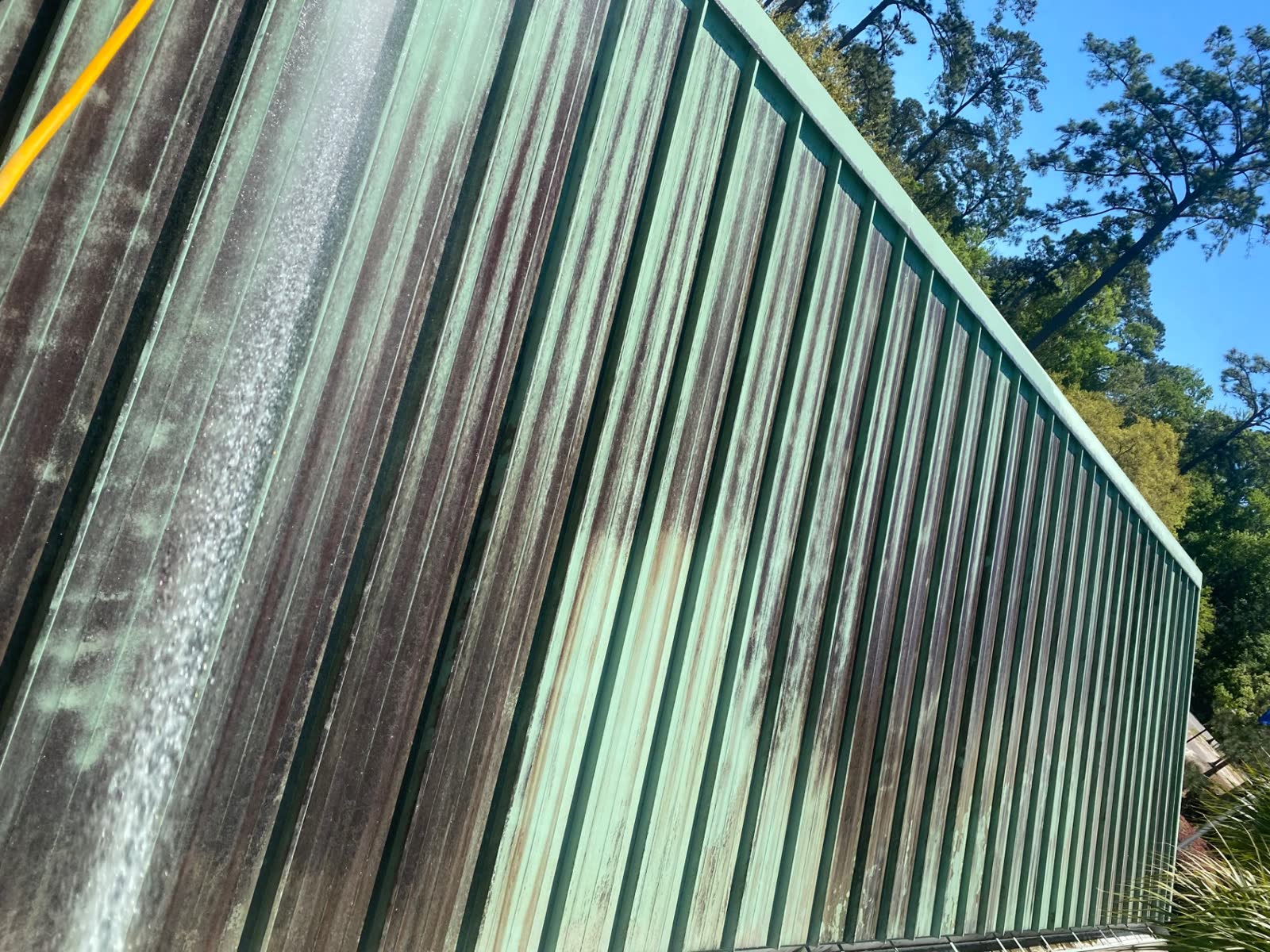 Green metal fence panels streaked with rust and mildew before cleaning